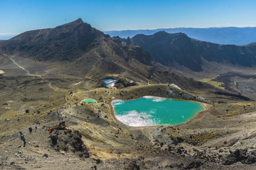 Hikers passing by the vibrant emerald hued lakes of Tongariro National Park.