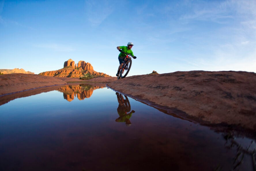 Mountain biker riding a slickrock trail with Cathedral Rock illuminated by sunset in the distance