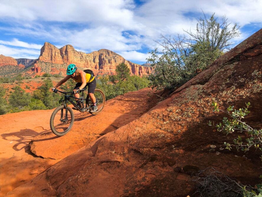 A female biker descending an exposed trail with great sandstone formations looming in the distance.